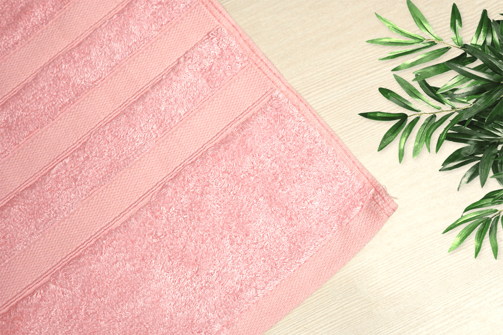Soft pink bamboo bath towel on a light wooden surface with green foliage, showcasing eco-friendly luxury.