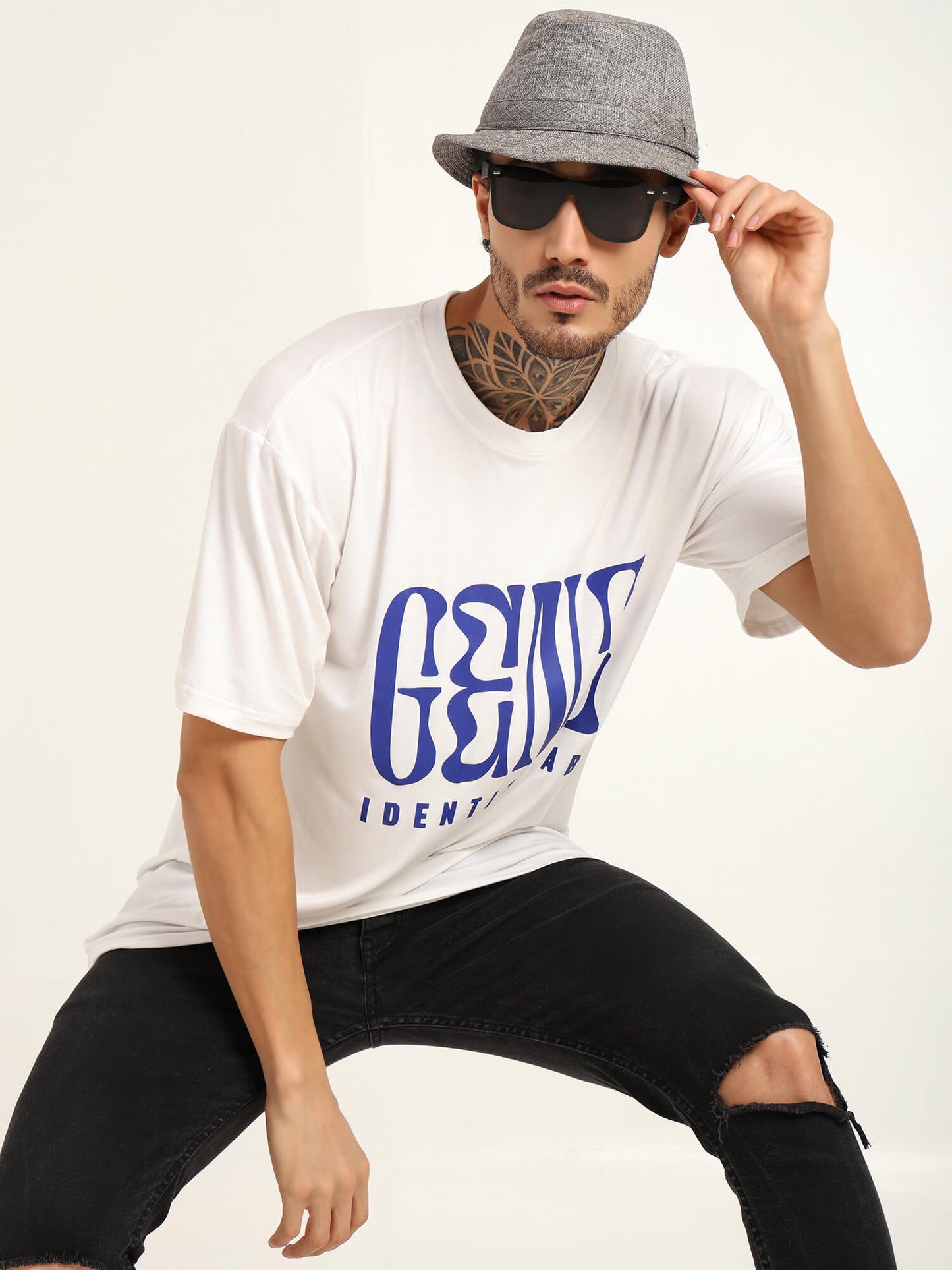 Men's oversized white T-shirt with blue graphic, styled with sunglasses and a gray hat for trendy streetwear.