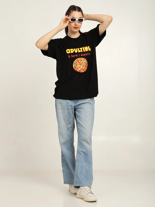 Person wearing a black t-shirt with a graphic design and text, light blue jeans, and white sneakers on a plain background.
