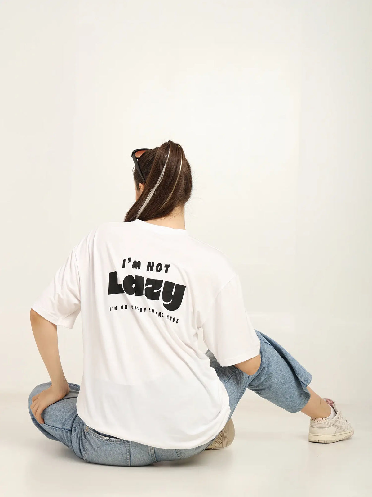 Woman wearing an oversized white T-shirt with 'I'm Not Lazy' graphic, styled casually with denim jeans.