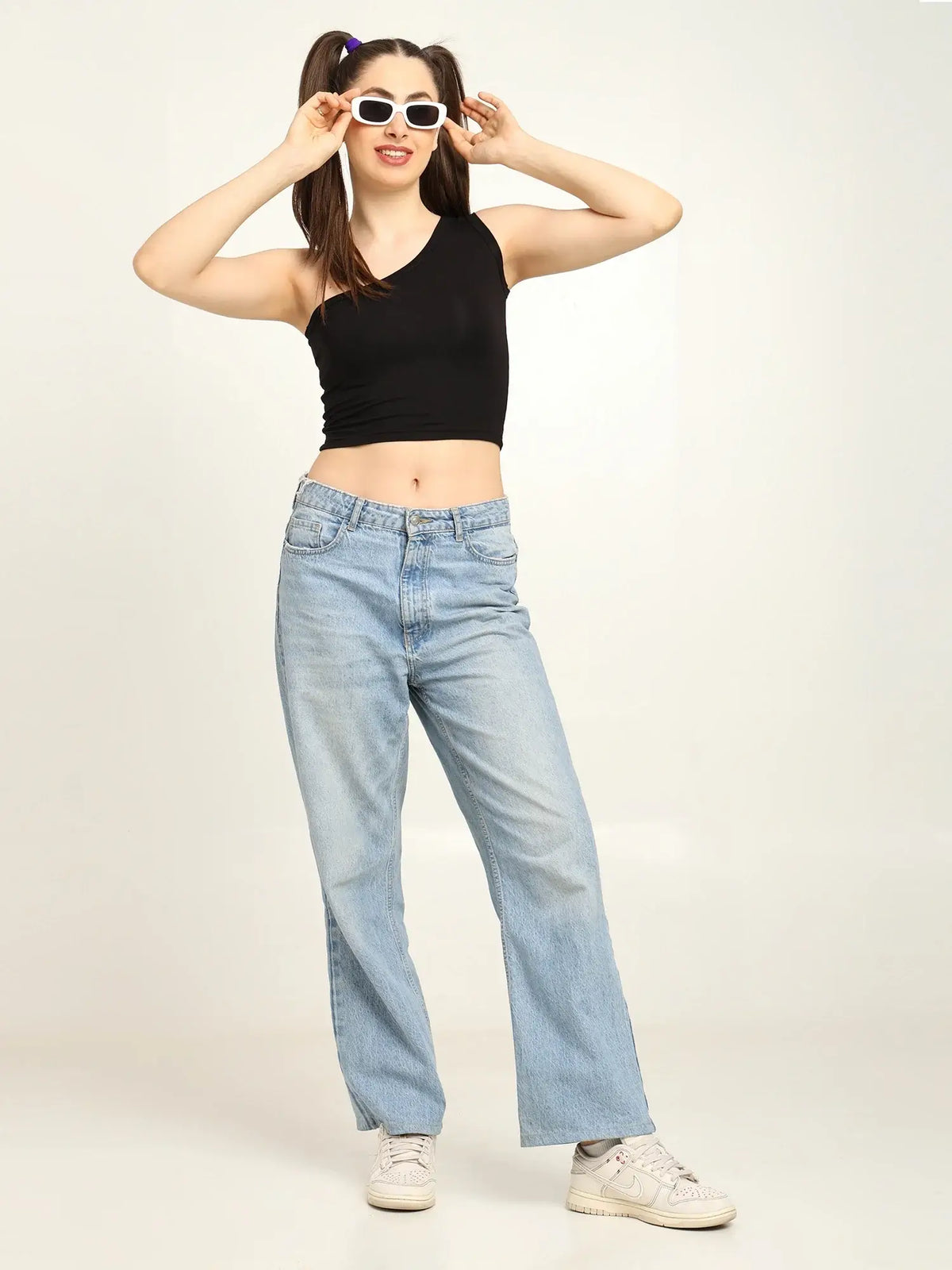 Gen Z woman in black one-shoulder bamboo top and light jeans, showcasing a trendy and casual spring style.