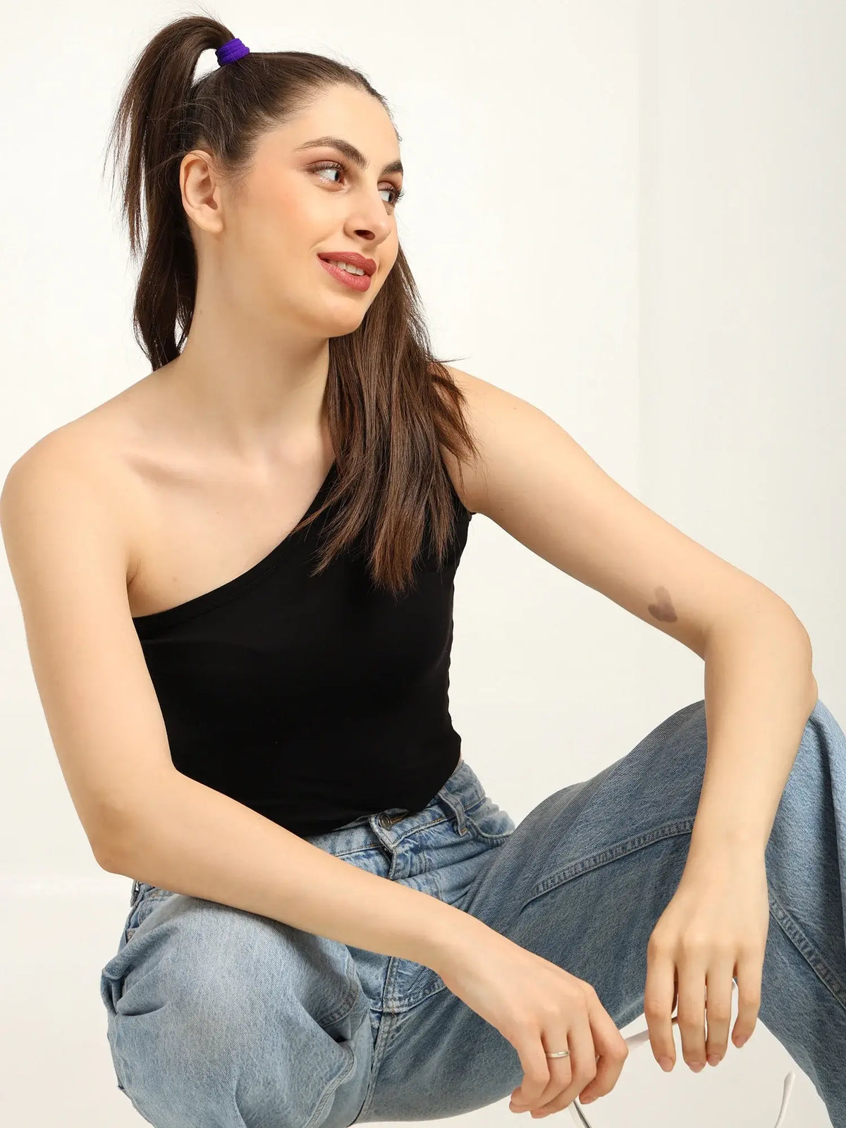 Gen Z model wearing a black one-shoulder bamboo top, styled with relaxed jeans and a playful ponytail.